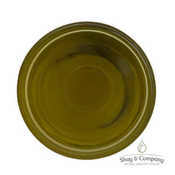 Top-down view of golden-green olive oil in a clear glass dish with Shay & Company logo watermark.