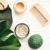 Zero waste flat lay. Natural eco friendly solid shampoo bar, wooden brush,  conditioner,soap, konjaku sponge on white wood with green monstera leaves.  Eco products plastic free